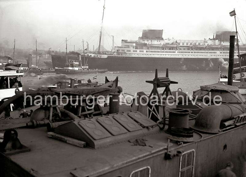 Vierschrauben Schnelldampfer EUROPA - Reederei Norddeutscher Lloyd; ca. 1930. Hamburgbilder als Fotoposter + Kunstdruck als Weihnachts- und Geburtstagsgeschenk zum Jubilaeumsgeschenk. 776_196a Der Passagierdampfer EUROPA wird von drei Schleppern von seinem Liegeplatz am Kai der Werft Blohm & Voss in den Vorhafen gezogen, um von dort aus seine Fahrt auf die Elbe aufzunehmen. Hinter dem Arbeitsschiff liegen Barkassen und Schiffe der Hafenrundfahrt mit Fahrgsten an Bord, die dem Schiffsmanver zusehen.