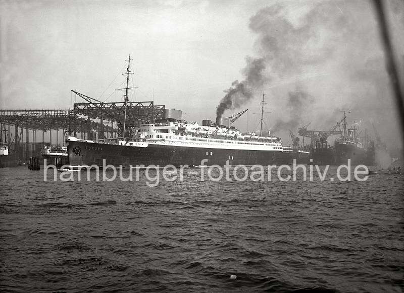 Alte Schiffsbilder -  Passagierdampfer EUROPA - Barkassenbegleitung, qualmende Schiffsschornsteine. Alte Hamburg Fotos als Firmengeschenk / Fotoleinwand oder Fotopapier. 780_199 Die EUROPA verlsst mit qualmenden Schornstein den Kai der Werft Blohm & Voss und startet seine Fahrt nach Bremerhaven um von dort die Jungfernfahrt nach New York zu unternehmen. Auf dem oberen Deck zwischen den beiden Schornsteinen befindet sich ein Katapult mit einem Schwimmflugzeug. Das Flugzeug diente der schnelleren Postbefrderung; es wurde 800 bis 1000 km vor dem Zielhafen von Bord gestartet.