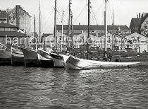 802_7 Mehrere Fischewer liegen im Fischereihafen Altona - die flachbodigen Schiffe sind mit Seitenschwertern versehen, mit denen eine Abdrift verringert wird. Durch den geringen Tiefgang knnen die Schiffe hervorragend auf den tideab- hngigen Gewssern der Elbe und ihren Nebenflssen manvrieren. Lks. ein Ausschnitt der Altonaer Fischauktionshalle und an der Groen Elbstrae Lagerhuser und Wohngebude. Auf dem Kais sind Fischkisten aus Holz gestapelt.