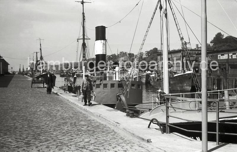 Alte Hamburger Altona-Bilder, Fischdampfer; Altonaer Fischereihafen, Ausrstungskai; ca. 1952. Geschenke zur Erinnerung: HamburgMotive als Kunstdruck auf Leinwand + Foto-Poster.  803_8 Fischdampfer liegen am Ausrstungskai des Fischereihafens Hamburg Altona; dort Bunkern die Dampfer Kohle und nehmen Eis zur Khlung des Fangs an Bord. Ein Fischer geht mit zwei Zink-Eimern zu seinem Schiff - eine einachsige Holzkarre / Schottsche Karrre steht auf dem Pflaster des Kais - auf der gegenberliegenden Seite des Hafenbeckens Lagerhuser. 
