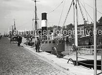 803_8 Fischdampfer liegen am Ausrstungskai des Fischereihafens Hamburg Altona; dort Bunkern die Dampfer Kohle und nehmen Eis zur Khlung des Fangs an Bord. Ein Fischer geht mit zwei Zink-Eimern zu seinem Schiff - eine einachsige Holzkarre / Schottsche Karrre steht auf dem Pflaster des Kais - auf der gegenberliegenden Seite des Hafenbeckens Lagerhuser. 