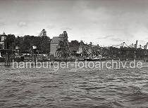 809_B_222 Blick ber die Elbe in den Altonaer Hafen. An dem Getreidespeicher steht in groen Lettern die Aufschrift "GETREIDE PFLEGE; H. PAULSEN". Die Getreideladung eines am Kai liegenden Dampfers wird ber die Sauganlage der beiden Getreideheber gelscht. Auf der Kaianlage liegen Fsser - auf den Gleisen der Hafenbahn stehen Khlwagen mit der Aufschrift "SEEFISCHE". Im Hintergrund der Kai des Altonaer Kohlehafens.