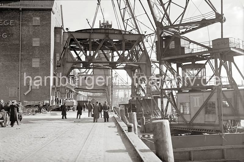 Alte Aufnahmen Altonas - Demontage ein Hafenkrans im Altonaer Hafen; ca. 1938. Altonaer Bilder auf FotoleinwandLeinwand + als Fotoposter. 813_B_350a Durch den Anschluss Altonas an Hamburg 1936 wurden auch die beiden Hfen Hamburg und Altonas koordiniert. In diesem Zusammenhang wird der 40 t Kran im Altonaer Hafen demontiert und am Rohft aufgestellt. Zwei Schwimmkrne hieven den Unterbau der Krananlage in die Luft. Mnner in Mnteln und mit Hten beobachten die Szene. An der Laderampe des Getreidesilos geht die Arbeit weiter, ein Anhnger wird mit Scken beladen.