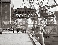 813_B_350a Durch den Anschluss Altonas an Hamburg 1936 wurden auch die beiden Hfen Hamburg und Altonas koordiniert. In diesem Zusammenhang wird der 40 t Kran im Altonaer Hafen demontiert und am Rohft aufgestellt. Zwei Schwimmkrne hieven den Unterbau der Krananlage in die Luft. Mnner in Mnteln und mit Hten beobachten die Szene. An der Laderampe des Getreidesilos geht die Arbeit weiter, ein Anhnger wird mit Scken beladen. 