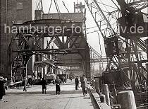 814_B_358a Durch den Anschluss Altonas an Hamburg 1936 wurden auch die beiden Hfen Hamburg. und Altonas koordiniert. In diesem Zusammenhang wird der 40t Doppellenker Wippkran am Kai des Altonaer Hafens abgebau und am Rohft wieder aufgestellt. Zwei Schwimmkrne hieven das Unterge- stell der Krananlage an. Im Hintergrund stehen an der Laderampe des Getredesilos beladene Lastwagen und Gterwaggons.