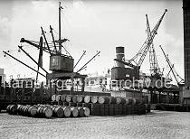 817_B_290a Ein Kaikran hievt Gefrierware auf das vor dem Neumhlener Khlhaus liegende Frachtschiff. Auf den Pflastersteinen des Hafenkais liegen Metallfsser, ein Teil ist in die bereit stehenden offenen Gterwagen / Rungenwagen verladen.