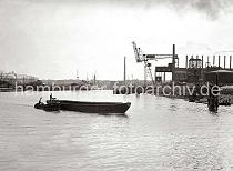 821_B_259 Eine Schute wird von der Barkasse HERTA aus dem Harburger Seehafen 3 auf die Sderelbe geschleppt; der Ewerfhrter steht auf dem Heck seines Lastkahns. Ein Seeschiff und ein Frachtsegler liegen an den Dalben des Hafenbeckens; hinter den Masten des Segelschiffs ist der Turm der Heimfelder Kirche St. Paulus zu erkennen.