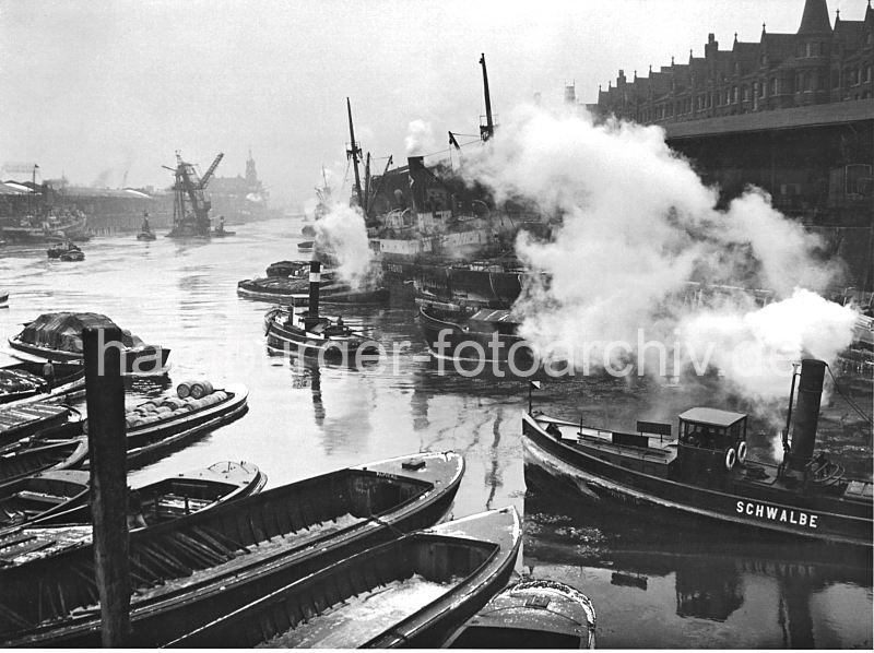 Sandtorhafen 1936 - Schiffe am Sandtorkai, Kohleheber - Schlepper unter Dampf.  173_3502 Frachter liegen am Sandtorkai, Schuten haben lngsseits fest gemacht - ein Schlepper unter Dampf kommt vom Brooktorhafen und fhrt in den Sandtorhafen ein. Vor dem Kaiserkai wird ein Kohleheber von zwei Schleppern gezogen - im Hintergrund die Silhouette vom Kaiserspeicher und die Mndung des Hafenbeckens in die Elbe. 