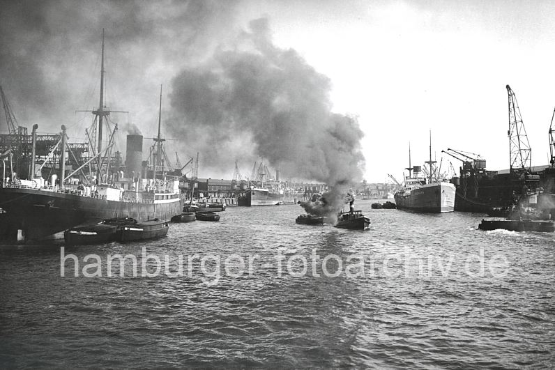 historische Hafenbilder - Baakenhafen 1931 - Frachter am Versmannkai + Petersenkai.  173_3502 Ein Frachter liegt am Versamannkai des Baakenhafens und wird entladen - ein Schlepper zieht eine Schute in der Mitte des Hafenbeckens, dicker Qualm steigt aus seinem Schonfstein. Rechts am Petersenkai liegt ein Schwimmkran und wartet auf seinen Arbeitseinsatz.