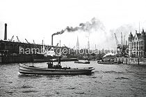 75_3502 Blick in den Magdeburger Hafen - ein Frachtschiff liegt am Fruchtschuppen C und wird entladen, der Schornstein hinter dem Schuppendach gehrt zum Gaswerk am Grossen Grasbrook. Hinter der Baakenbrcke die Dcher der Hamburger Speicherstadt und die Kirchtrme der St. Nikolai und St. Katharinenkirche. Rechts das Backstein-Verwaltungsgebude vom Furchtschuppen am Versmannkai - ein Wasserboot ist mit Frischwasser auf seiner Versorgungsfahrt.