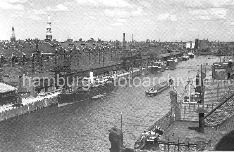 265_607a Blick vom Kaispeicher A in den Sandtorhafen; ein Frachter liegt am Sandtorkai und wird mit einem Halbportalwippkran entladen. Die gelschte Fracht wird in den Kaischuppen gelagert oder in die dahinter liegenden Lagerbden der Speicherstadt transportiert. Links im Hintergrund der Kirchturm der St. Jakobikirche und daneben die St. Katharinenkirche. Rechts die Backsteinarchitektur vom Kaispeicher B am Magdeburger Hafen.