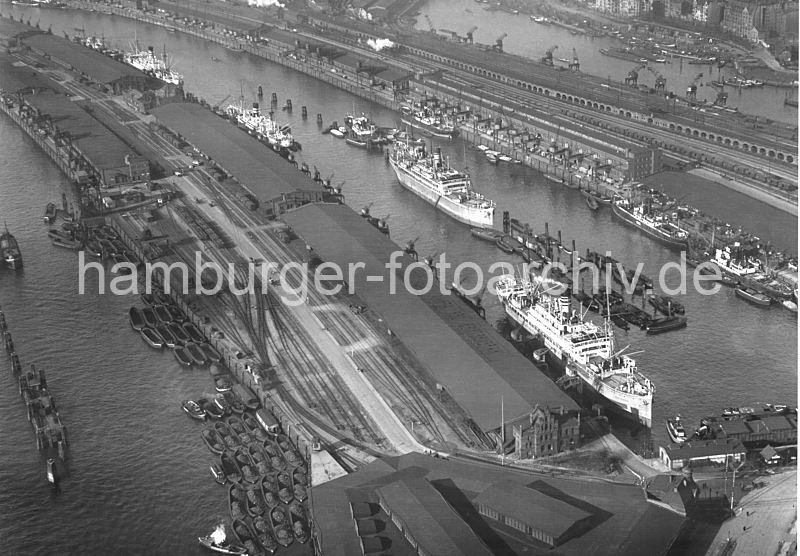 Luftaufnahme vom Hamburger Hafen ca. 1932  - Baakenhafen, Petersenkai + Versmannkai  268_1698 Luftaufnahme vom Baakenhafen und Norderelbe. Schuten liegen am Kirchenpauerkai; die Lastkhne werden mit Kohle beladen - auf dem Kai umfangreiche Gleisanlagen der Hafenbahn. Am Petersenkai des Baakenhafens liegen Frachtschiffe, die dort be- und entladen werden. Ein weiterer Frachter liegt in der Mitte des Hafenbeckens an den Dalben. Hinter den Lagerschuppen am Versmannkai ist die Pfeiler-Bahnstrecke mit den typischen Backsteinarkaden, davor verluft eine Strecke der Hamburger Hafenbahn, eine Lokomotive fhrt dort unter Dampf. Im Hintergrund ein Ausschnitt vom Oberhafen-Kanal mit der Schleuse zum Mittelkanal in Hamburg Hammerbrook.