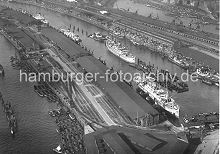 268_1698 Luftaufnahme vom Baakenhafen und Norderelbe. Schuten liegen am Kirchenpauerkai; die Lastkhne werden mit Kohle beladen - auf dem Kai umfangreiche Gleisanlagen der Hafenbahn. Am Petersenkai des Baakenhafens liegen Frachtschiffe, die dort be- und entladen werden. Ein weiterer Frachter liegt in der Mitte des Hafenbeckens an den Dalben. Hinter den Lagerschuppen am Versmannkai ist die Pfeiler-Bahnstrecke mit den typischen Backsteinarkaden, davor verluft eine Strecke der Hamburger Hafenbahn, eine Lokomotive fhrt dort unter Dampf. Im Hintergrund ein Ausschnitt vom Oberhafen-Kanal mit der Schleuse zum Mittelkanal in Hamburg Hammerbrook.