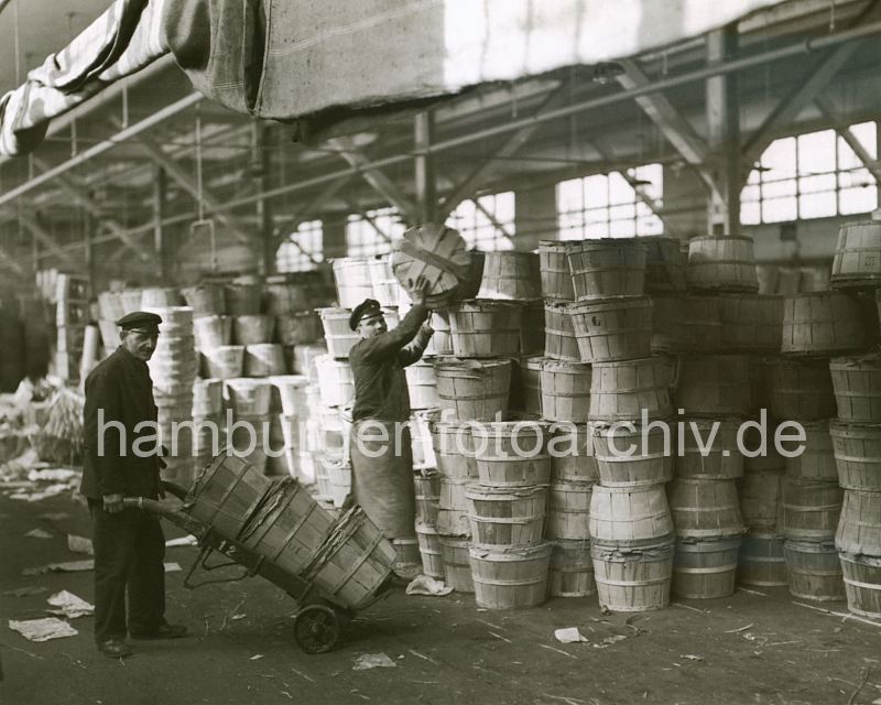 historische Hafenfoto aus Hamburg - Hafenarbeiter mit Sackkarre im Fruchtschuppen ca. 1930.  308_420a Die Arbeiter im Fruchtschuppen A am Baakenhafen, einem der vielen Hafenbecken des Hamburger Hafens, transportieren die Fsser mit Sackkarren vom Hafenkai zum Stauraum. Dort wird die empfindlichen Fracht von Hand gestapelt. 