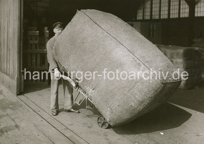309_421 Der grosse Ballen wird vom Lagerarbeiter auf einer Sackkarre von der Laderampe aufgenommen und in das Innere des Lagerschuppens transportiert.