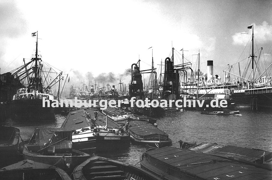 0953976 alte Fotos von Hamburg - alte Hamburger Bilder : Blick in den  Hamburger Segelschiffhafen ca. 1930, links wird ein Frachtschiff am Americakai mit Krnen entladen - Motorschiffe und Lastkne liegen mit ihrer abgedeckten Ladung im Hafenbecken. In der Bildmitte entladen zwei Getreideheber einen Frachter und beladen lngsseits liegende Khne mit dem Getreide.