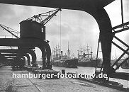 0953978 Krne am Amerikakai im Segelschiffhafen des Hamburger Hafens - ein Gterwagen der Hafenbahn steht auf den Gleisen am Kai und wird beladen. Fsser aus Holz liegen auf den Pflastersteinen und warten darauf in die am Kai liegenden Schuten verladen zu werden. Schiffe liegen auf Reede, fest gemacht an den Duckdalben aus Holzstmmen, im Hintergrund sind die Masten zweier Segelschiffe, Frachtsegler zu erkennen.