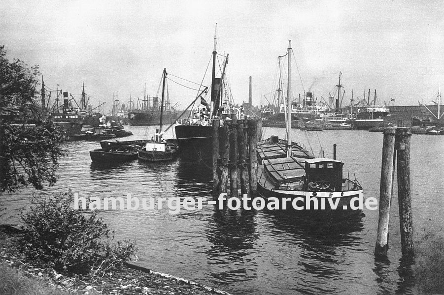 0953984 hamburg Bilder vom Hamburger Hafen Fotos der Hafenstadt -  Blick vom Lbecker Ufer in den Hansahafen - im Hintergrund die Schornsteine der Frachtschiffe die am Oswaldkai liegen und deren Ladung gelscht wird. Im Vordergrund hlzerne Duckdalben, die aus langen Baumstmmen gerfertigt werden, die tief in den Hafengrund gerammt werden. An ihnen hat ein Motor-Binnenschiff und ein Dampfschiff festgemacht - das Binnenschiff hat seine Ladeluken mit Brettern abgedeckt, die die Ladung schtzen sollen; beim Frachter haben Lastkhne lngsseits fest gemacht, die die Fracht an Bord nehmen. 