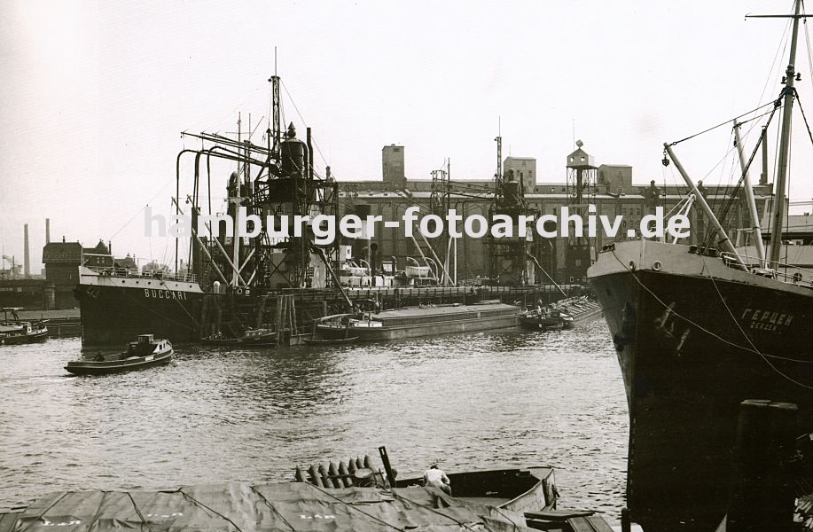 0953994 EinGetreidefrachter liegt an der Pier im Kuhwerder Hafen; die langen Saugrssel des Getreidehebers sind in den Laderaum des Frachters gesteckt und befrdern die Ladung an Land. Auf der anderen Seite des Stegs liegen Binnenschiffe, die ber eine Schttvorrichtung beladen werden knnen. Eine Barkasse fhrt Richtung Kaianlage - lks. im Hintergrund die Ellerholzschleuse, die Grevehove Schleuse. Diese Schlickschleuse fhrt zum Reiherstieg.