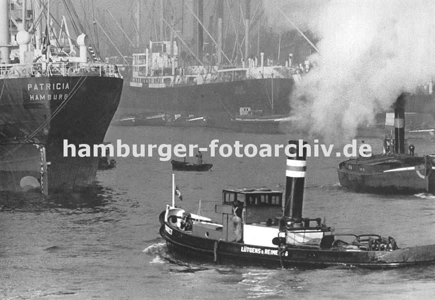 0953995 Frachtschiffe liegen im Kaiser-Wilhelm-Hafen - im Vordergrund dampft ein Hafenschlepper durch das Hafenbecken; lks. wird ein Binnenschiff von einem Schlepper geschleppt, dicker Qualm steigt aus dem Schornstein des Arbeitsschiffes. In der Bildmitte fhrt ein Tuckerboot, der Schiffer fhrt im Stehen, um einen besseren berblick ber das Geschehen auf dem Wasser zu bekommen. 