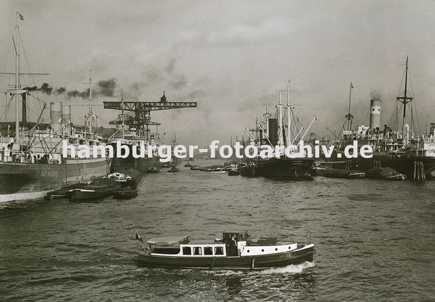 0954005 Blick in das Hamburger Hafenbecken vom Rosshafen - links der Vulcankai, im Hintergrund sind dort die Werkhallen der Vulcanwerft zu erkennen. Weit ausladende Krne stehen an der Kaianlage, mit denen die Frachter gelscht oder beladen werden. Im Vordergrund fhrt eine Barkasse Richtung Rosskai. Rechts oben liegen Frachter, Leichter und Schuten in der Mitte vom Rosshafen an den Dalben. 