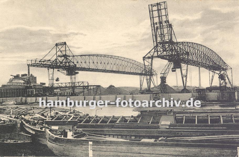 0954021 Im Harburger Seehafen wird mit weit ausladende Krananlagen Schttgut von den an der Kaimauer liegenden Schuten gelscht. Im Vordergrund liegen leere Lastkhne, die Abdeckung des Laderaums ist entfernt. 