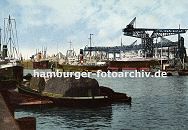 k_119689 hstorische Ansicht Hafen Hamburg : Blick ber den Kuhwrder Hafen - eine Schute lieg hoch beladen am Hafenkai, ihre Ladung ist mit Netzen gesichert - auf der gegenber liegende Seite werden mit einer weit ausladenden Krananlage Frachtschiffe gelscht. 