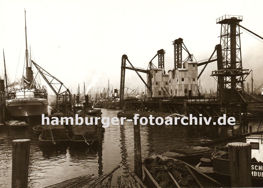 k_119690 Blick in den Kuhwrder Hafen - dicht gedrngt liegen die Schiffe in dem Hamburger Hafenbecken; rechts die stationre pneumatische Anlage, um das Schttgut wie z.B. Getreide aus den Frachtschiffen zu lschen. Im Vordergrund Duckdalben, die aus Nadelholz-Baumstmmen angfertigt sind und tief in den Hafengrund getrieben, den Schiffen zum anlegen oder festmachen dienen. Das Ende dieser dicken Pfhle ist mit Metall belegt, damit kein Wasser in die Stirnseite der Stmme dringen kann.