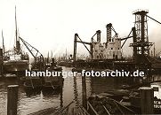 k_119690 alte Bilder aus Hamburg : Blick in den Kuhwrder Hafen - dicht gedrngt liegen die Schiffe in dem Hamburger Hafenbecken; rechts die stationre pneumatische Anlage, um das Schttgut wie z.B. Getreide aus den Frachtschiffen zu lschen. Im Vordergrund Duckdalben, die aus Nadelholz-Baumstmmen angfertigt sind und tief in den Hafengrund getrieben, den Schiffen zum anlegen oder festmachen dienen. Das Ende dieser dicken Pfhle ist mit Metall belegt, damit kein Wasser in die Stirnseite der Stmme dringen kann.