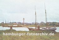 k_0954025 Blick über das Köhlfleet nach Finkenwerder; am Ufer liegt ein Segelschiff vor Anker, ein anderes hat den den Dalben fest gemacht. Im Hintergrund die Finkenwaerder Landungsbrücken an der eine Hafenfähre angelegt hat - zwischen den Häusern Finkenwerders ragt der Wasserturm heraus. 