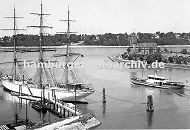 0954027 Blick von Finkenwerder Richtung Elbe ca. 1939; ein Segelschiff liegt am Steg - es ist mit Tauen an den Duckdalben fest gemacht. Eine Hafenfhre hat von den Finkenwerder Landungsbrcken abgelegt und fhrt Richtung Elbe. Dahinter ist das Hamburger Lotsenhaus zu erkennen, das von Hamburgs Oberbaudirektor Fritz Schumacher entworfen wurde. Am anderen Elbufer sind Huser an der Elbchaussee von Hamburg Othmarschen zu erkennen