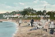 09540365 Badestrand am Elbufer von Blankenese ca. 1900; Mdchen in Kleidern stehen im Sand, andere bauen eine Sandburg. Eine Mutter liegt mit Kleid im Sand, dahinter ein Mann mit Anzug. Im Hintergrund die Huser von Blankenese und der Sllberg.