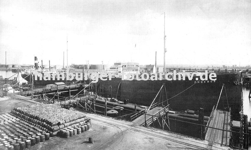 0954036 ein Tanker liegt im Hamburger Petroleumhafen am Kai - an Land sind Fsser gestapelt. Auf der gegenber liegenden Seite des Hafenbeckens sind runde Tanks zu erkennen.