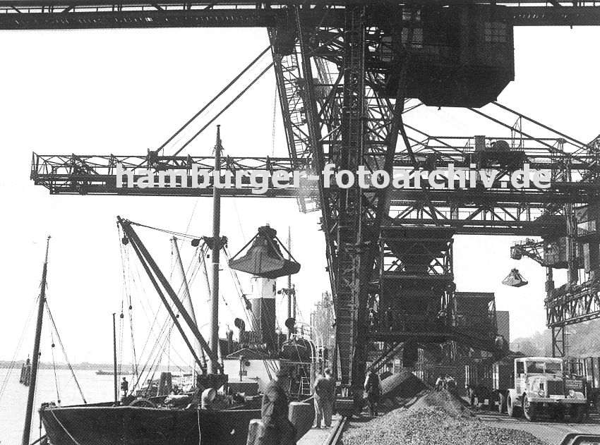 0954041 historisches Foto von Hamburg Altona - Kohlekai am Altonaer Hafen; der Greifer der weit ausladenden Krananlage holt die Kohle aus dem Laderaum des Frachters  und ldt seine Fracht am Kai ab. Dort lieg die Kohle in Bergen  - ein Lastwagen mit grossem Anhnger wartet darauf mit Kohle beladen zu werden