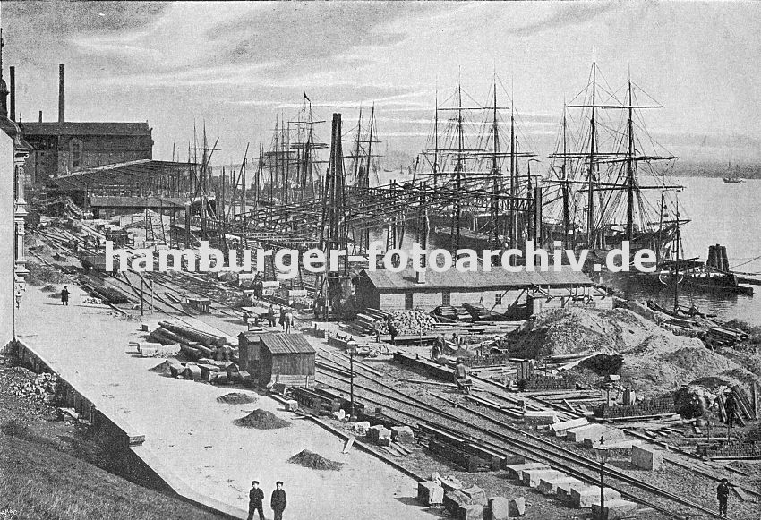 0954044 alte Hamburgbilder vom historischen Hamburg Altoana Bauarbeiten am Altonaer Hafenkai ca. 1905; Baumaterialien wie Bretter, Holzstmme und Sand liegen am Elbufer. Dazwischen verlaufen die Schienen der Hafenbahn, im hinteren Bereich stehen Gterwaggons. Mehrere Frachtsegler liegen mit ihren hohen Masten an dem Schiffsanleger.