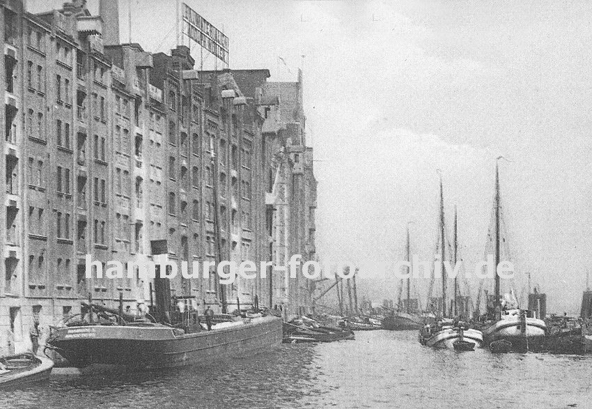 0954050 Blick auf die historische Hafenarchitektur der Speicher und Lagergebude im Hafen von Altona; ein Motor-Binnenschiff wird mit Scken beladen, die ber die Winde am Dach des Lagerhauses auf das Schiff transportiert wird. Auch die am Ponton liegenden Schuten werden mit Scken beladen - rechts Fischerboote an den Dalben des Altonaer Hafens.