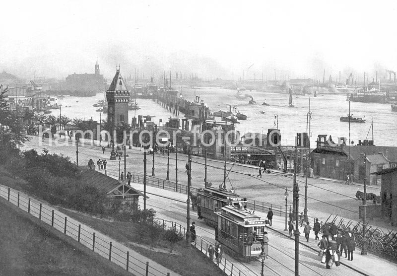 historisches Foto St. Pauli Landungsbrcken - Strassenbahnen, Pegelturm + Kaiserspeicher  0954069_26 St. Pauli Landungsbrcken ca. 1900 - zwei Strassenbahnen an der Haltestelle Landungsbrcken; ein Arbeiter trgt mehrere Milchkannen, ein anderer transportiert ein Fass auf der Handkarre. Leere Karren sind an der Strasse abgestellt. Hinter dem Pegelturm / Uhrturm ist die Silhouette des Kaispeichers A / Kaiserspeichers zu erkennen. Sie mchten dieses Motiv z.B. auf Fotoleinwand erwerben? www.hamburg- bilder.biz