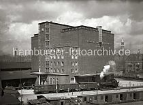 01158_105 Die Architektur des Khlhauses am Hbenerkai des Grasbrookhafens wurde vom Hamburger Oberbaudirektor Fritz Schumacher entworfen; an der Stirnseite des Treppenhauses ist das Hamburger Wappen weit sichtbar unter dem Dach angebracht. An der Seite der Khlhalle steht der Schriftzug " Gesellschaft fr Markt- u. Khlhallen, Werk 5, Hafenkhlhaus". Ein Lok der Hafenbahn zieht unter Dampf drei geschlossene Gterwaggons ber die Gleise; rechts im Hintergrund stehen Khlwaggons mit der Aufschrift "Seefische" und "Khlwagen". Vor dem Eingang, auf dem die Skulptur eines Fischers aufgestellt ist, steht ein Lastwagen, auf dessen Anhnger Holzfsser gestapelt sind. Im Vordergrund neben dem Fahrradschuppen liegen zerbrochene Holzfsser und -kisten.