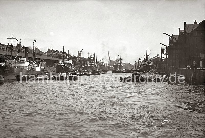 01173_2_228a Blick in den Sandtorhafen; rechts der Kaiserkai - beladenen Schuten liegen am Kai, die Ladung ist mit Persenning abgedeckt. Im Hintergrund hinter dem Frachtschiff und Schwimmkran die Silhouette des Kaispeichers B. Am Sandtorkai liegt u.a. der Dampfer INDALSALFVEN . Ein Ewerfhrter klettert gerade von seiner Schute ber ein Strickleiter an Bord des Frachtschiffs. Hinter dem Dach des Kaischuppens die Giebel und Winden der Speicherstadt. Bilder aus dem historischen Hamburger Hafen - Hafenbecken Sandtorhafen, Sandtorkai + Kaiserkai; ca.1934. 