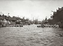 01173_2_228a Blick in den Sandtorhafen; rechts der Kaiserkai - beladenen Schuten liegen am Kai, die Ladung ist mit Persenning abgedeckt. Im Hintergrund hinter dem Frachtschiff und Schwimmkran die Silhouette des Kaispeichers B. Am Sandtorkai liegt u.a. der Dampfer INDALSALFVEN. Ein Ewerfhrer klettert gerade von seiner Schute ber ein Strickleiter an Bord des Frachtschiffs. Hinter dem Dach des Kaischuppens die Giebel und Winden der Speicherstadt.