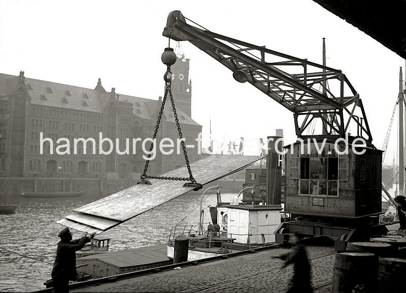 Bilder aus dem historischen Hamburger Hafen - Arbeit am im Sandtorhafen / Sandtorkai, Hafenkran; ca.1934. 01175_63 Am Sandotorkai des Sandtorhafens werden Blechplatten mit einem Hafenkran verladen - mit einem speziellen Anschlag hebt der Kran die Fracht in die Hhe, um sie auf das am Kai liegende Schiff zu verladen. Ein Hafenarbeiter dirigiert die Fracht mit den blossen Hnden. Im Hintergrund die Seitenansicht des Kaispeichers A am Kaiserkai.