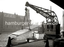 01175_63 Am Sandotorkai des Sandtorhafens werden Blechplatten mit einem Hafenkran verladen - mit einem speziellen Anschlag hebt der Kran die Fracht in die Hhe, um sie auf das am Kai liegende Schiff zu verladen. Ein Hafenarbeiter dirigiert die Fracht mit den blossen Hnden. Im Hintergrund die Seitenansicht des Kaispeichers A am Kaiserkai.