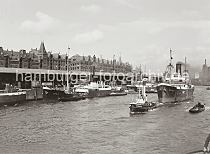 01179_618 Das Frachtschiff Frachter REIHER wird vom Schlepper CAROLINE  aus dem Sandtorhafen Richtung Elbe geschleppt. Aus den Schornsteinen beider Schiffe steigt Qualm. Im Hintergrund re. ein Ausschnitt des Kaispeichers B am Magedburger Hafen.  Am Sandtorkai liegen die Schiffe GREIF und MEISE - ihinter den Dchern der Lagerschuppen 4 + 5 ragt die Fassade der neogotischen Speicherstadt mit den Giebeltrmen und Winden unter den Dchern hervor.