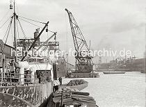 01180_533 Ein Schwimmkran mit einer Holzkiste am Haken liegt lngsseits eines Frachters im Sandtorhafen (?) - das Wasser des Hafenbeckens ist eisbedeckt. Im Vordergrund ist der Frachter DELPHIN, beladene Schuten liegen lngsseits.