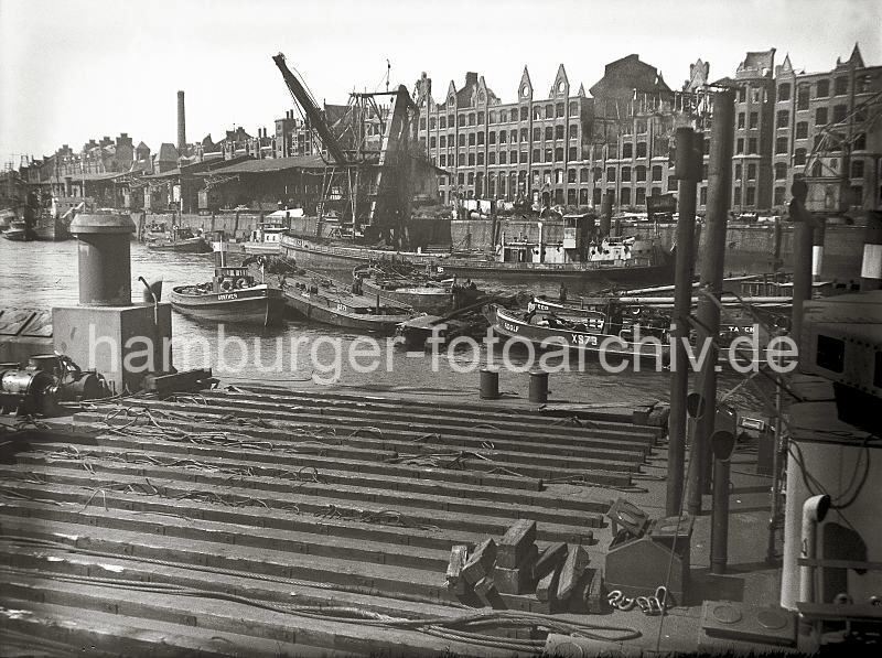 Bilder zur Geschichte des Sandtorhafens. Kriegszerstrung im Hafen Hamburg - Fassade der zerbombten Speicherstadt; ca.1948. Hafenfotos auf Leinwand mit Keilrahmen und FotoPoster. 02199_2 Mit Hilfe von Schuten und Barkassen wird eine durch Kriegseinwirkungen ins Hafenwasser gestrzte Lokomotive der Hafenbahn im Sandtorhafen zum Schwimmkran geschleppt. Am Sandtorkai liegen Arbeitsboote und ein anscheinend beschdigter Kohlenheber. Die leeren Giebel der Speichergebude ragen in den Himmel - ein Schornstein des Kesselhauses ist zerstrt.