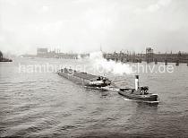 02218_636 Der Schlepper OTTO zieht einen Oberlnder Kahn ber die Norderelbe - im Hintergrund das Gasometer der Gaswerke auf dem Grasbrook und rechts der Kirchenbauerkai. Im Elbstrom sind in regelmssigen Abstnden Holzdalben aufgestellt, an denen die Schiffe anlegen knnen. Hinter den Dchern der Kaischuppen sind die Ausleger der Krne im Baakenhafen zu erkennen.