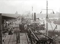 02228_793a Blick auf hinteren Abschnitt des Baakenhafen mit dem Schuppen 25 am Versmannkai. Ein Rollkran beldt einen Frachter mit Ballen - Kaiarbeiter bereiten auf der Laderampe den Transport weiterer Gter vor. In dem offenen Kaischuppen sind Kisten, Tonnen und Scke gelagert - der Zugang wird nachts mit einem Eisentor versperrt. Im Hintergrund sind in der Bildmitte und rechts die Bgen der Elbbrcken zu erkennen und auf der linken Bildseite der niedrige Zinnenturm des Schleusenwrterhauses der Baakenschleuse, die zum Oberhafen / Billehafen fhrt. 