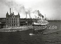 02235_152 Blick ber den Magdeburger Hafen zum Versmannkai des Hamburger Baakenhafens. Der Dampfer NATIA hat am Kai fest gemacht -  Qualm steigt aus seinem Schornstein. Auf der Kaianlage transportieren Kaiarbeiter Fruchtkisten mit der Sackkarre in den Fruchtschuppen A - eine Hieve Kisten wird vom Kran auf der Rampe abgesetzt.