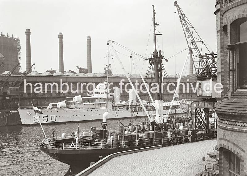 Schiffe im Magdeburger Hafen - Frachtschiff + Marinetransporter; ca. 1938. Hamburger Hafenarchiv der HHLA / Hamburger Fotoarchiv Christoph Bellin.  02251_767 Im Vordergrund rechts das Verwaltungs-Ziegelgebude der Fruchtschuppen im Baakenhafen. Am vorderen Kai des Magdeburger Hafens liegt ein kleines Kstenmotorschiff das auf seinem Deck Fsser geladen hat. Am gegenber liegenden Kai vor dem Kaischuppen D liegt ein Marinetransporter und dahinter sind die Schornsteine und Gasometer der Gasanstalt auf dem Groen Grasbrook zu sehen.