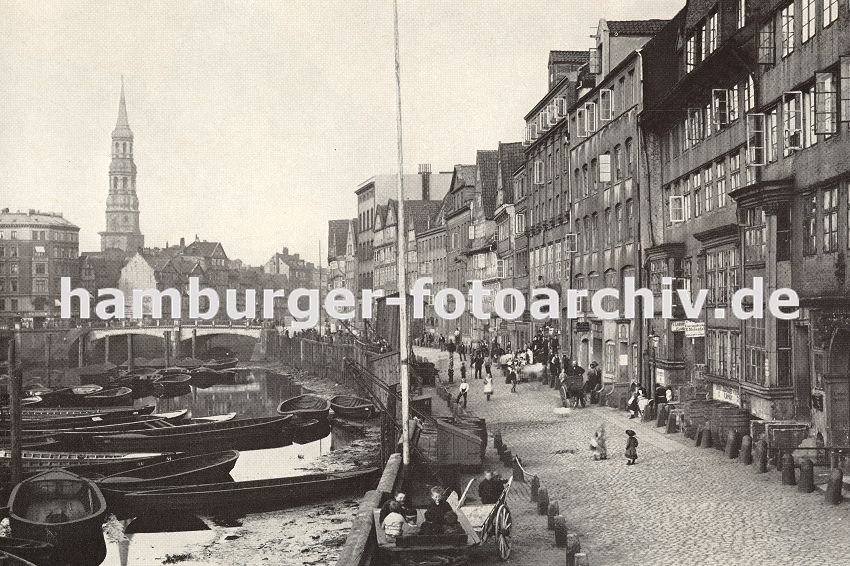 01147712 Hamburgensien / Hamburgs Geschichte :: Blick ber Kehrwieder Richtung Kirchturm der St. Katharinenkirche. Es ist Ebbe im Hamburger Binnenhafen und die Boote liegen im Schlick fest. Kinder spielen auf der Strasse, die mit Kopfstein gepflastert ist - Fsser stehen auf der Strasse vor einer Weinhandlung. Durch den Zollanschluss Hamburgs 1888 an Preuen entstand der Hamburger Freihafen - ca. 20 000 Menschen, die auf den Elbinseln Kehrwieder, Brook und  Wandrahm lebten, mussten ihre Wohnungen und Arbeitspltze verlassen und sich nach neuem Wohnraum umsehen - die Gebude wurden fr den Neubau der Speicherstadt abgerissen. 